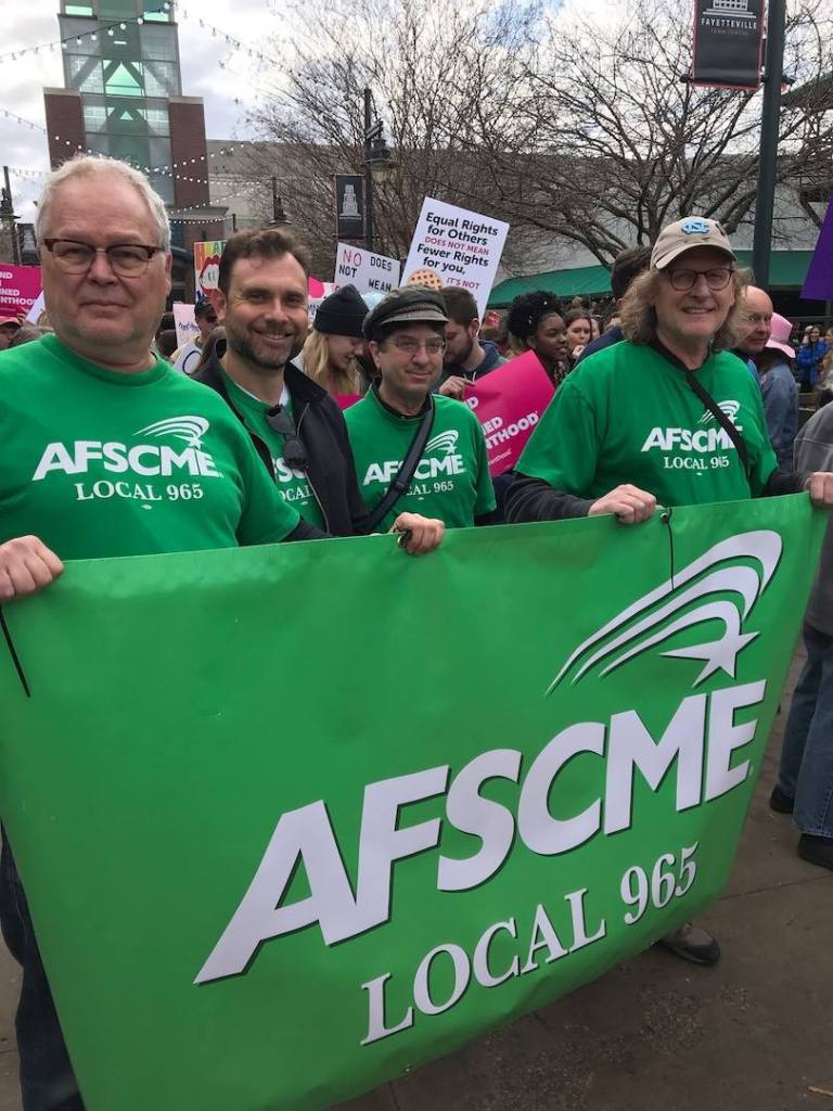 From left, Ted Swedenburg, Bret Schulte, Ben Pollock and Steve Boss hoist the Local 965 banner Feb. 2 at the 2019 NWA Women's March in downtown Fayetteville.