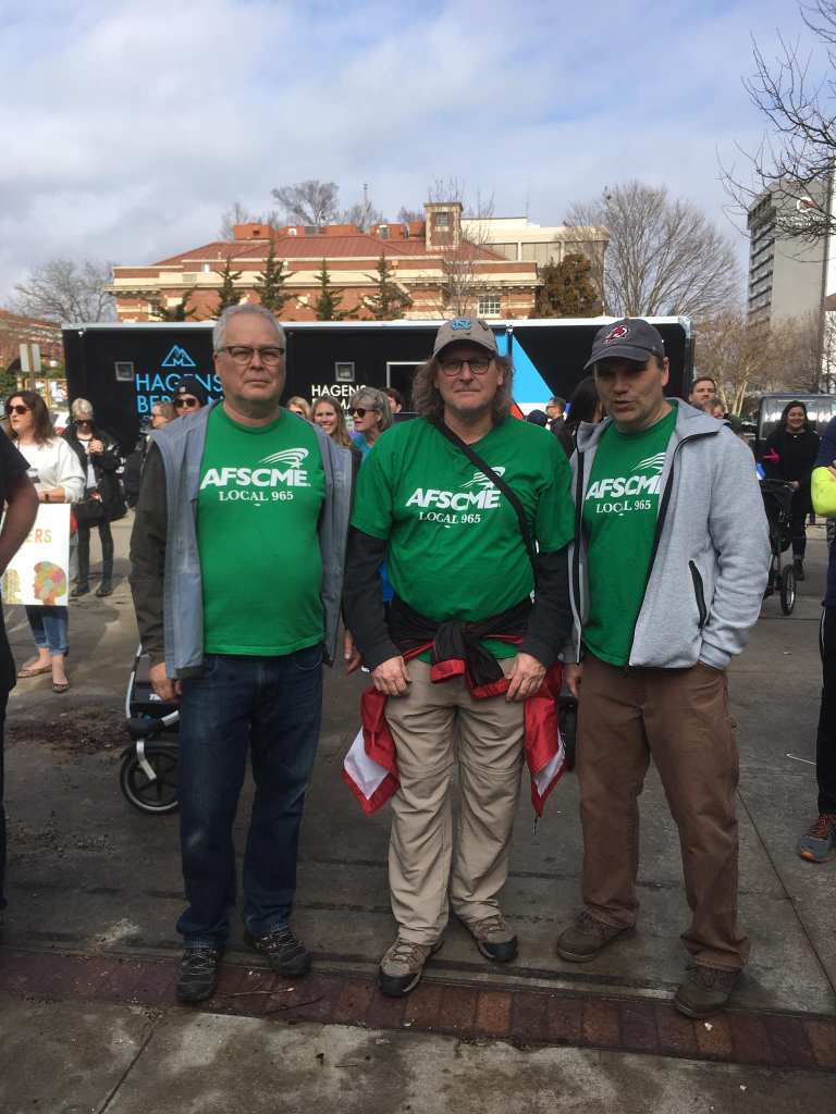 From left, Ted Swedenburg, Steve Boss and Mike Pierce listen to speakers at the rally that preceded the 2019 NWA Women's March, Feb. 2 in downtown Fayetteville.